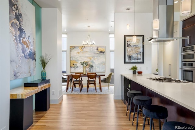 kitchen with island range hood, pendant lighting, light hardwood / wood-style flooring, and a breakfast bar