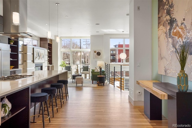 kitchen with pendant lighting, appliances with stainless steel finishes, a kitchen breakfast bar, light wood-type flooring, and floor to ceiling windows