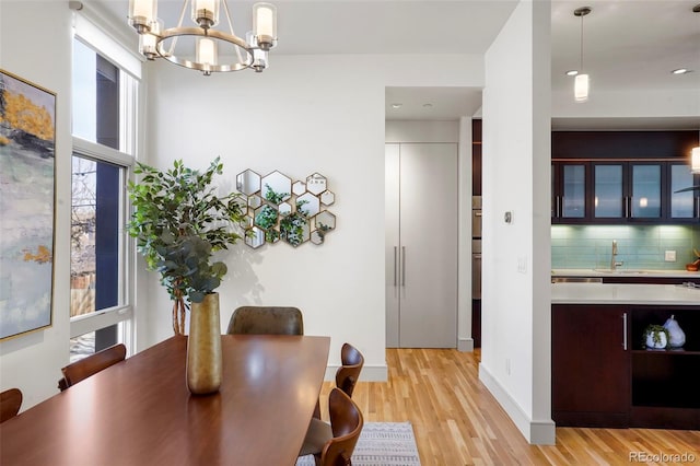 dining room with light wood-type flooring, a healthy amount of sunlight, sink, and a notable chandelier