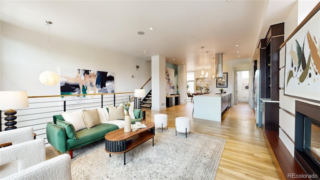 living area with recessed lighting, stairway, light wood finished floors, and an inviting chandelier