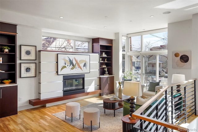 living room with wood finished floors, a wall of windows, a glass covered fireplace, and recessed lighting