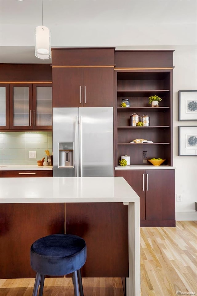 kitchen with light wood-style flooring, light countertops, stainless steel refrigerator with ice dispenser, a kitchen bar, and pendant lighting