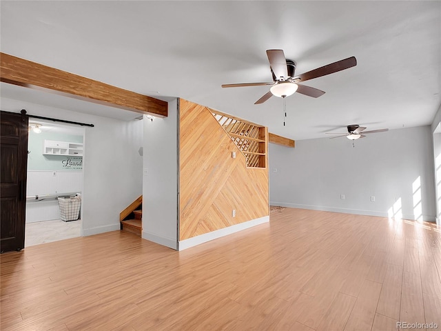 unfurnished living room with stairs, a barn door, light wood-style floors, and beam ceiling