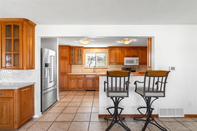 12940 W 75th Ave, Arvada, CO 80005 - kitchen with appliances with stainless steel finishes, brown cabinets, light countertops, backsplash, and glass insert cabinets