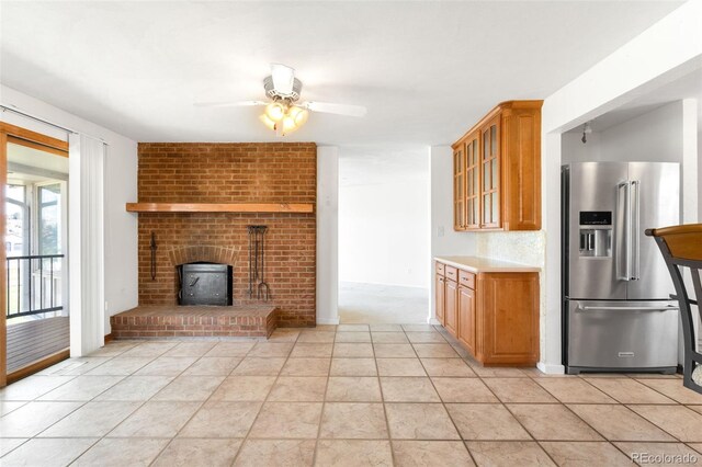 12940 W 75th Ave, Arvada, CO 80005 - kitchen featuring stainless steel fridge, ceiling fan, glass insert cabinets, light countertops, and a brick fireplace