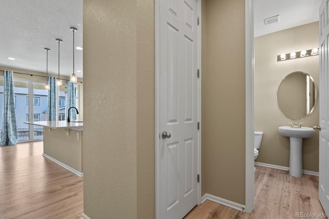 hall featuring light wood-type flooring, baseboards, a textured wall, and a sink