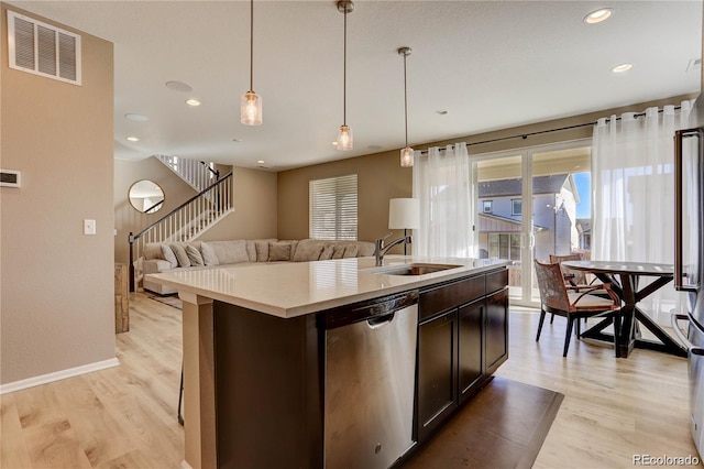 kitchen with dishwasher, a sink, light wood-style floors, open floor plan, and light countertops