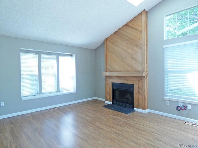 9669 W Chatfield Ave Unit A, Littleton, CO 80128 - unfurnished living room featuring vaulted ceiling, healthy amount of natural light, a fireplace, wood finished floors, and a textured ceiling