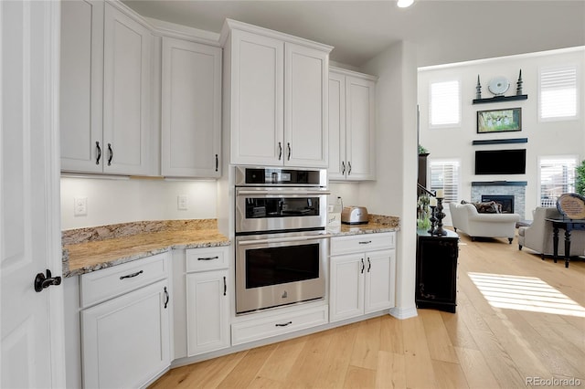 kitchen featuring white cabinetry, double oven, a wealth of natural light, and light hardwood / wood-style flooring