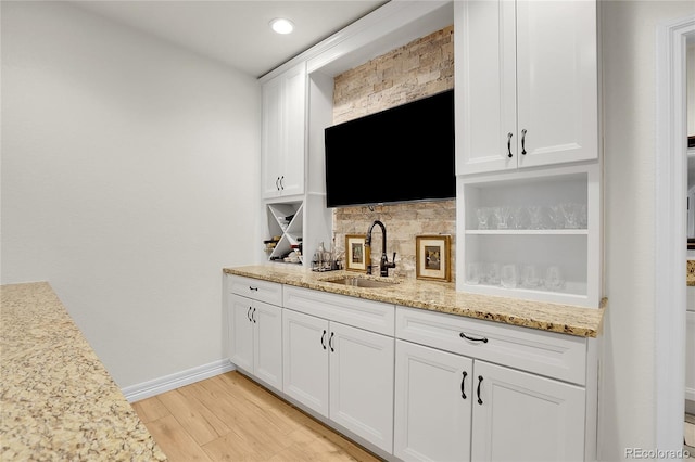 bar with sink, white cabinetry, light stone countertops, light hardwood / wood-style floors, and decorative backsplash