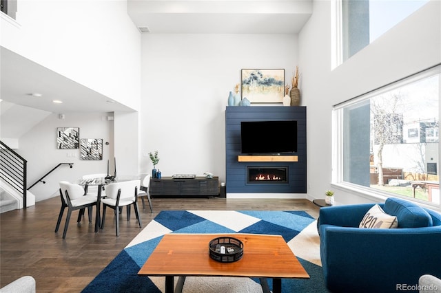 living area featuring wood finished floors, a towering ceiling, and a lit fireplace