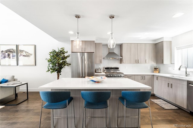 kitchen featuring wall chimney range hood, a sink, a breakfast bar area, backsplash, and appliances with stainless steel finishes