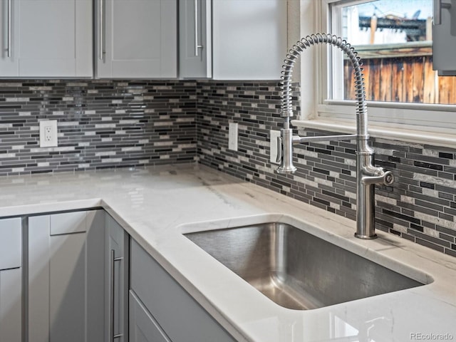 kitchen featuring gray cabinets, light stone counters, decorative backsplash, and a sink
