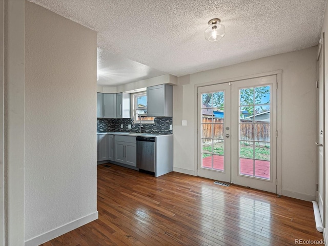 kitchen with baseboards, decorative backsplash, dark wood-type flooring, stainless steel dishwasher, and visible vents