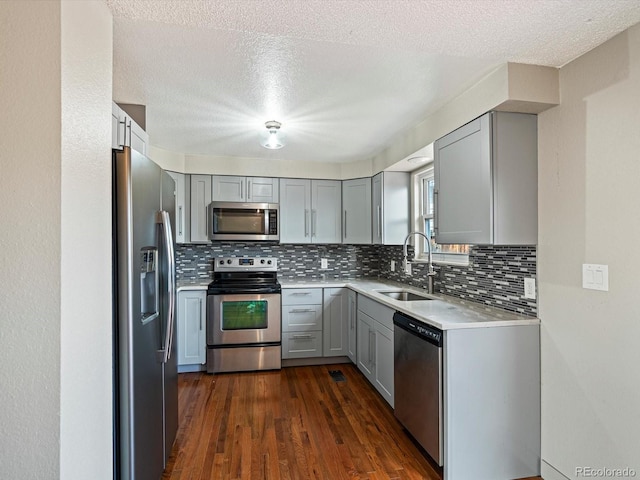 kitchen featuring decorative backsplash, dark wood-style flooring, gray cabinets, a sink, and stainless steel appliances