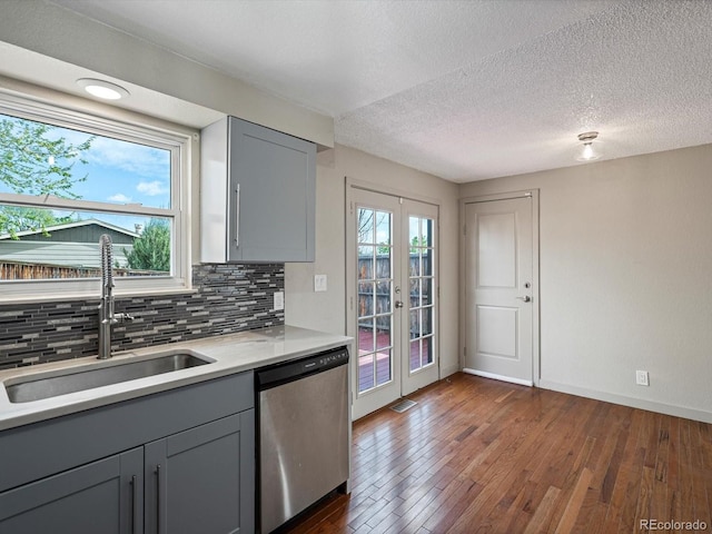 kitchen featuring stainless steel dishwasher, a sink, backsplash, and gray cabinetry