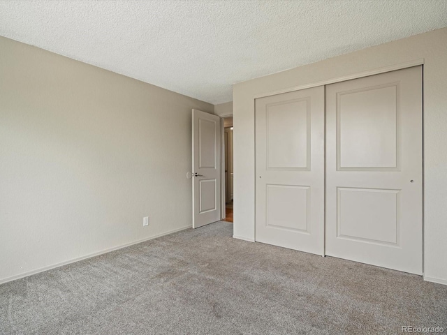 unfurnished bedroom with a closet, carpet flooring, a textured ceiling, and baseboards