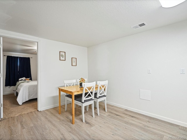 dining room featuring baseboards, light wood-type flooring, a textured ceiling, and visible vents
