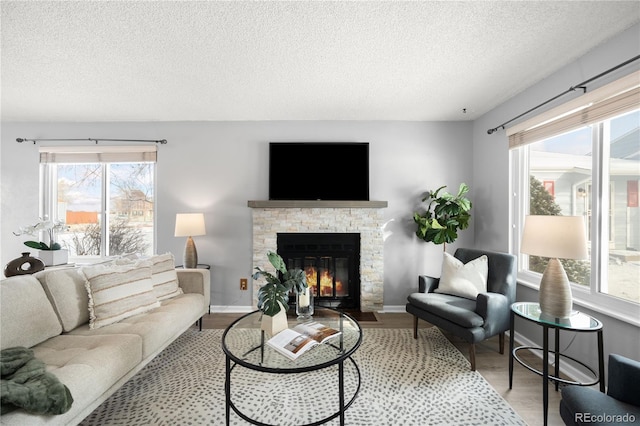 living room with hardwood / wood-style flooring, a stone fireplace, and a textured ceiling