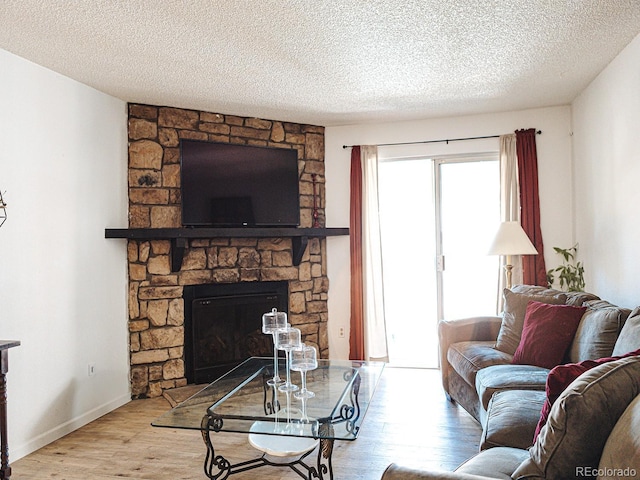 living room with light wood-type flooring, a textured ceiling, and a stone fireplace