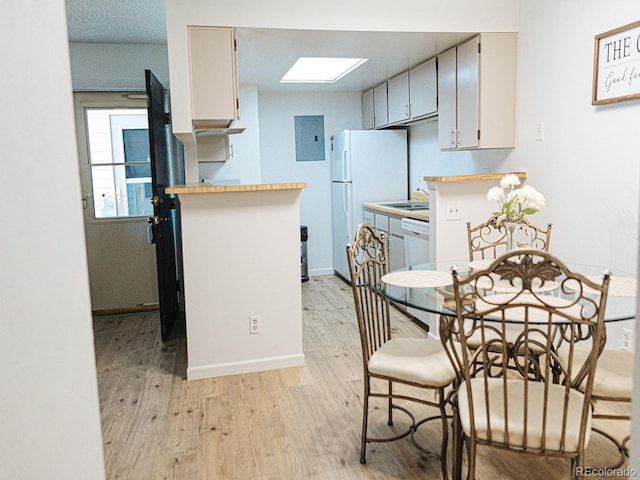 kitchen featuring kitchen peninsula, light wood-type flooring, a skylight, white appliances, and electric panel