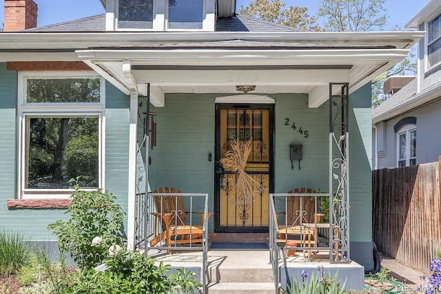 2445 N Franklin St, Denver, CO 80205 - view of exterior entry featuring a porch, roof with shingles, a chimney, and brick siding
