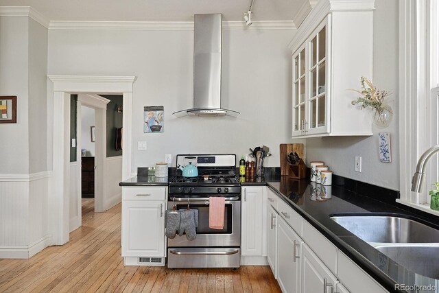 2445 N Franklin St, Denver, CO 80205 - kitchen with gas range, wall chimney range hood, dark countertops, ornamental molding, and glass insert cabinets