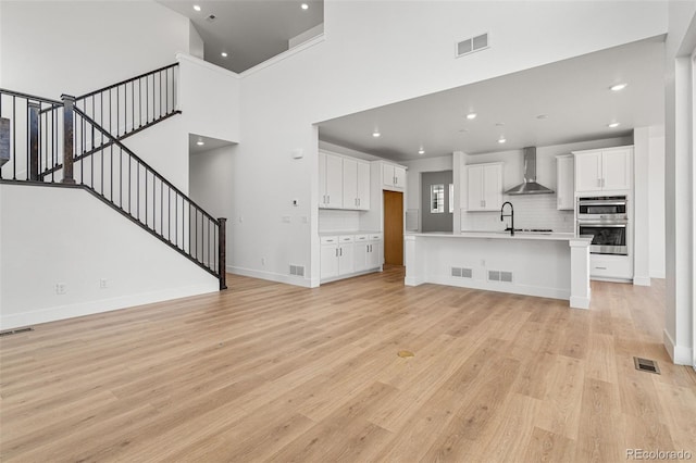 unfurnished living room featuring a high ceiling, sink, and light hardwood / wood-style floors