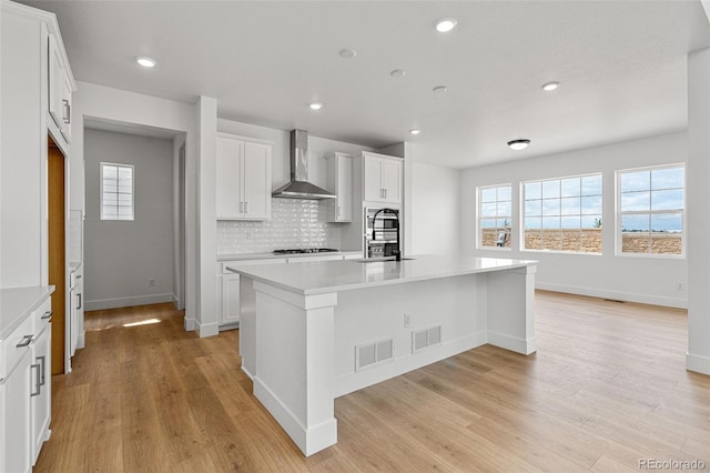 kitchen featuring light wood-type flooring, a center island with sink, white cabinets, and wall chimney range hood