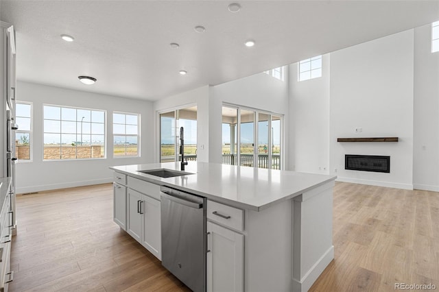 kitchen featuring dishwasher, white cabinets, an island with sink, and sink