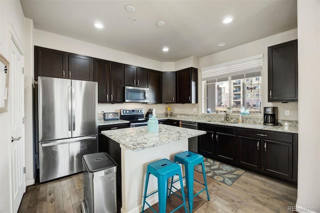 kitchen featuring a center island, a kitchen bar, light wood-style floors, stainless steel appliances, and a sink