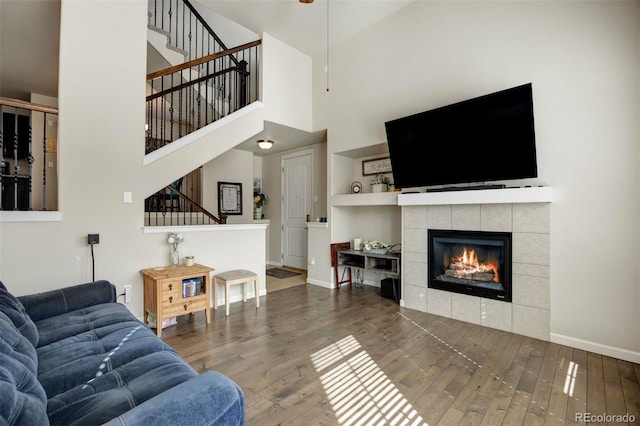 living area featuring baseboards, stairs, a tile fireplace, a high ceiling, and wood finished floors