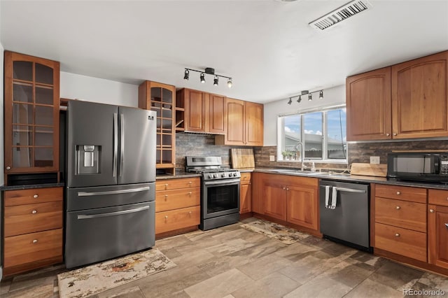 kitchen featuring a sink, visible vents, appliances with stainless steel finishes, dark countertops, and glass insert cabinets