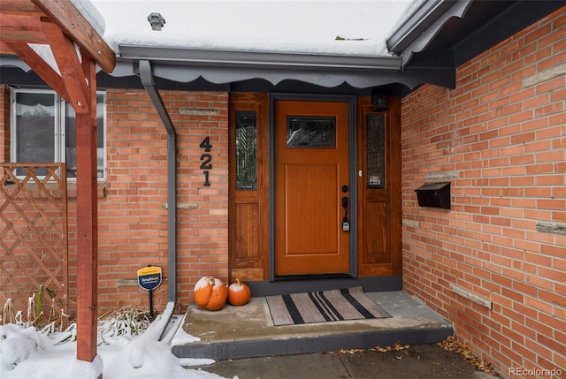 snow covered property entrance featuring brick siding