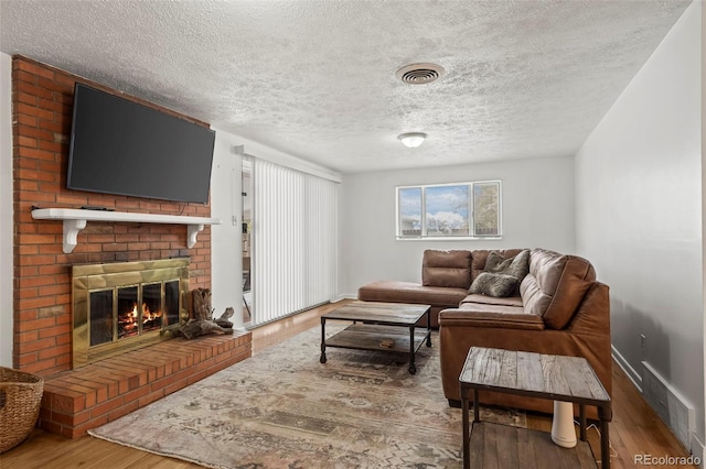 living room with hardwood / wood-style flooring, a textured ceiling, and a brick fireplace