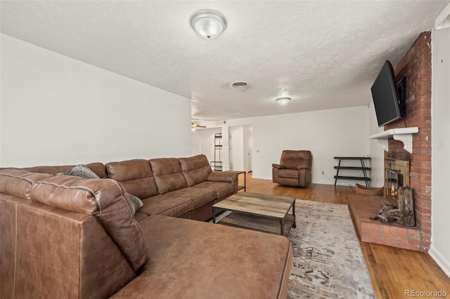 living room featuring a textured ceiling, hardwood / wood-style flooring, a brick fireplace, and ceiling fan