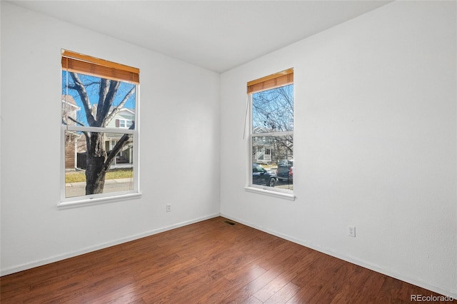 empty room with a wealth of natural light and hardwood / wood-style flooring