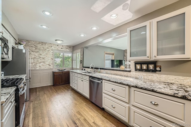8600 W 2nd Ave, Lakewood, CO 80226 - kitchen featuring appliances with stainless steel finishes, a sink, wainscoting, light stone countertops, and glass insert cabinets