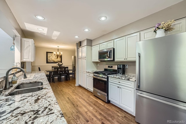 8600 W 2nd Ave, Lakewood, CO 80226 - kitchen featuring appliances with stainless steel finishes, a sink, a chandelier, light stone counters, and light wood-type flooring