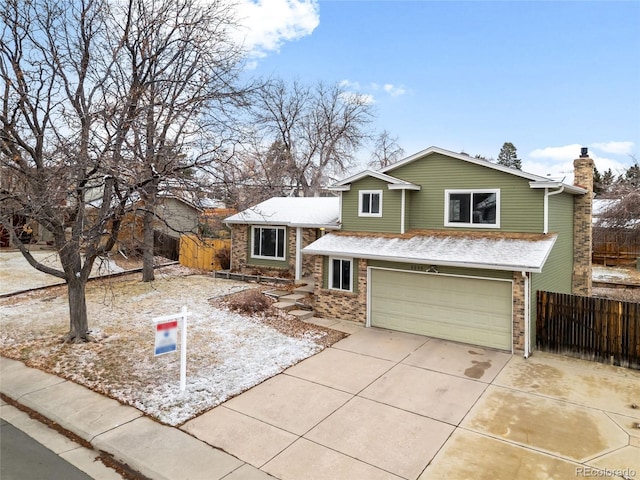 split level home with a garage, concrete driveway, brick siding, and fence