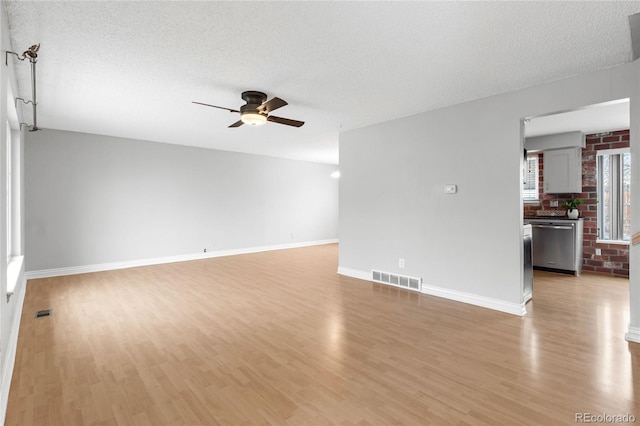 empty room with light wood-type flooring, ceiling fan, visible vents, and a textured ceiling