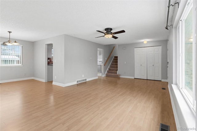 unfurnished living room with stairs, light wood finished floors, visible vents, and a ceiling fan