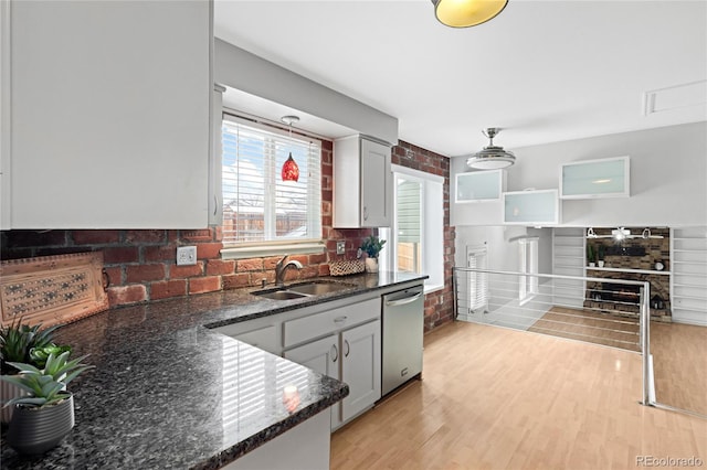 kitchen with a sink, light wood-type flooring, dishwasher, tasteful backsplash, and dark stone countertops