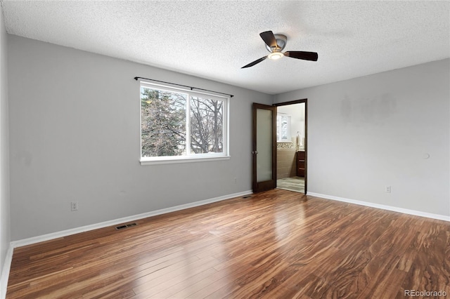 spare room featuring a textured ceiling, wood finished floors, visible vents, and baseboards