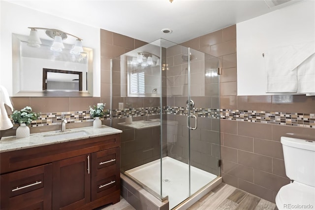 full bath with tasteful backsplash, toilet, vanity, a shower stall, and tile walls