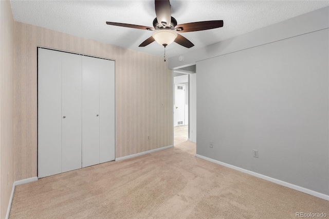 unfurnished bedroom featuring a closet, light colored carpet, a textured ceiling, and baseboards