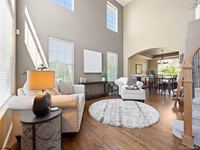 living area with arched walkways, a towering ceiling, wood finished floors, and a chandelier