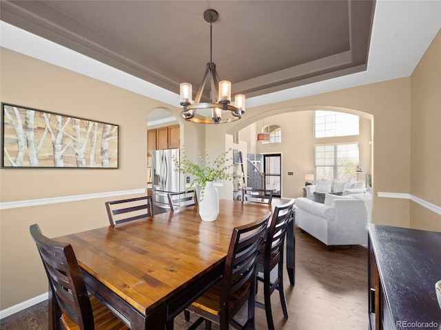 dining space with arched walkways, a chandelier, a raised ceiling, and dark wood-type flooring