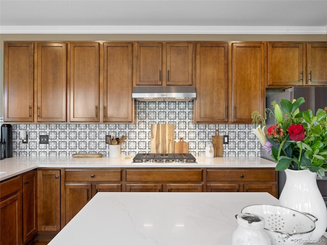 kitchen with under cabinet range hood, stainless steel appliances, ornamental molding, and brown cabinetry