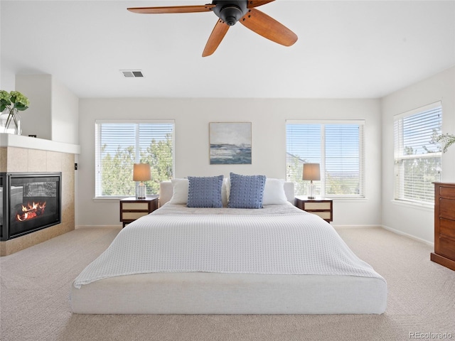 carpeted bedroom with a tiled fireplace, baseboards, and a ceiling fan